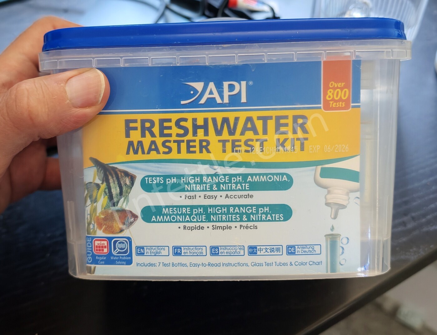 Hand holding a well-used API Freshwater Master Test Kit tub with the label and expiry stamp visible