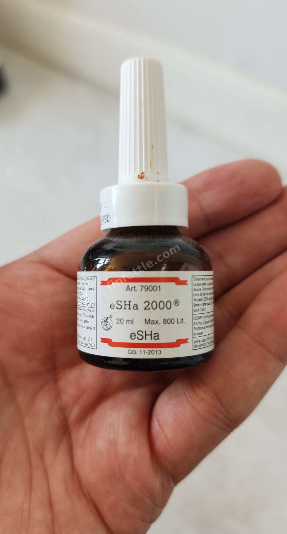 Hand holding a small brown 20 ml dropper bottle of eSHa 2000 aquarium treatment with a white nozzle